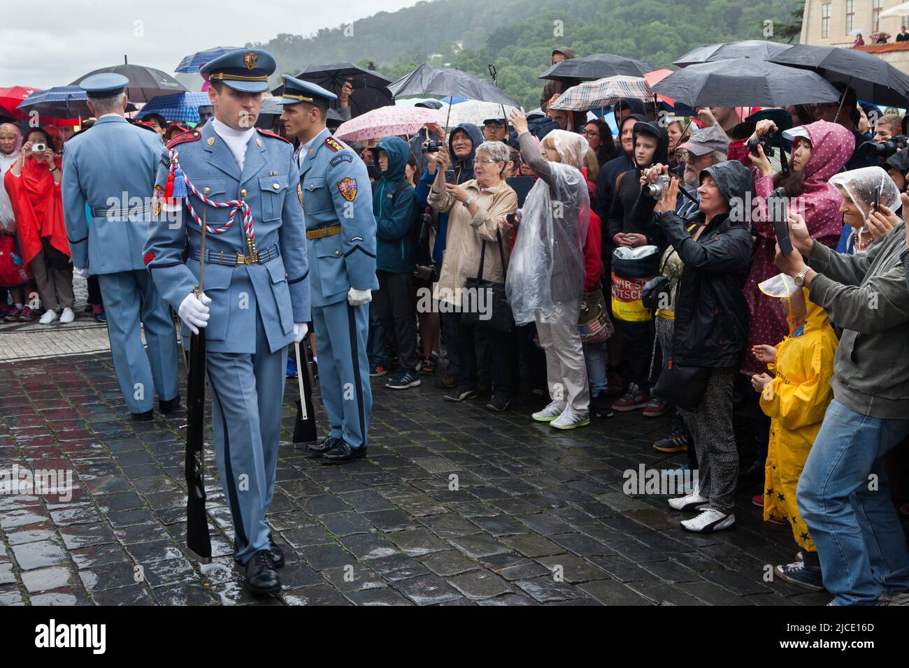 I turisti osservano la cerimonia del Cambio della Guardia del Castello (Hradní stráž) sotto la pioggia di fronte al Castello di Praga in Piazza Hradčanské a Praga, Repubblica Ceca. Foto Stock