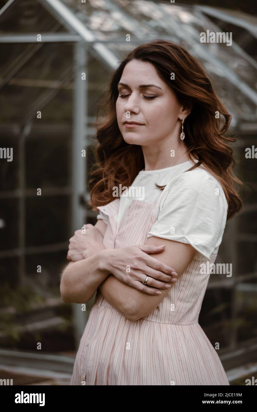 Bella donna al suo 30s nel giardino sera scuro. Bella donna ricci da sogno in serata camminando in abito lungo sopra serra. Moda Foto Stock