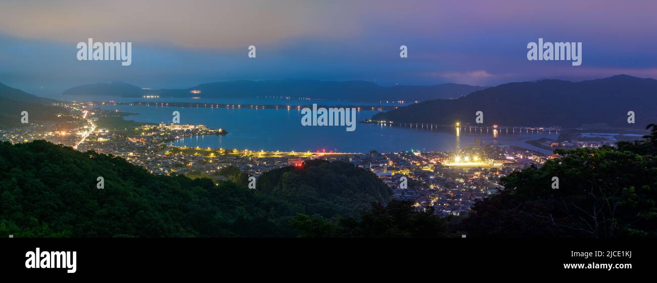 Vista panoramica di Amanohashidate e delle luci della città con il tramonto che si illumina nel cielo Foto Stock