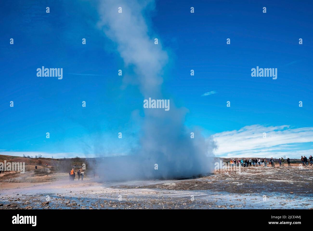 Esploratori che guardano l'eruzione del geyser Strokkur nella valle contro il cielo blu Foto Stock