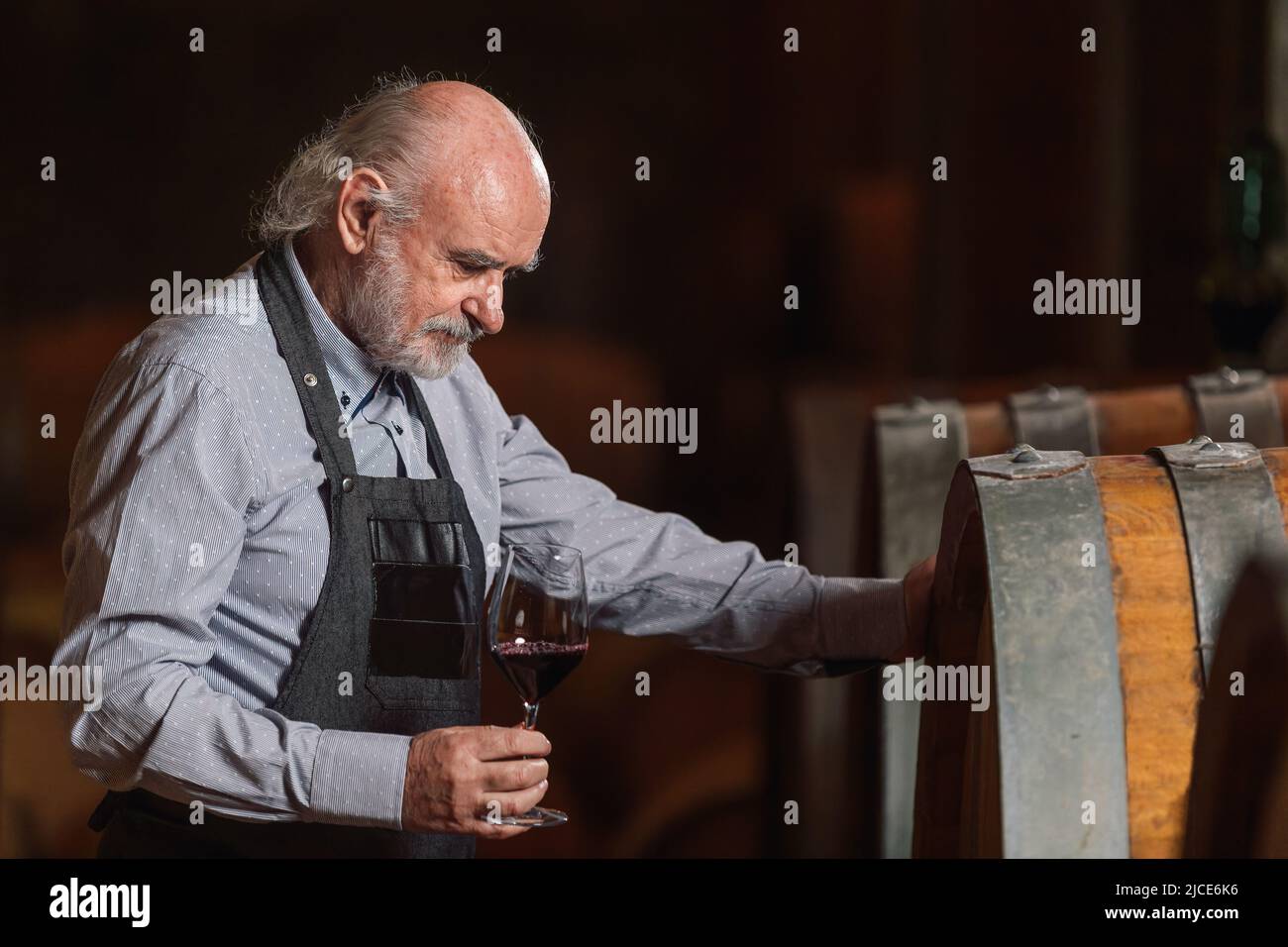 Produttore di vino senior presso l'azienda vinicola che controlla i barili in cantina. Foto Stock