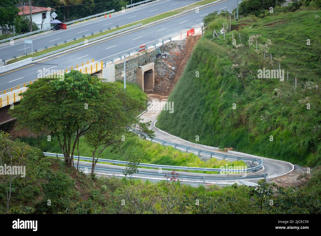 Strada stretta sotto un ponte dove passano le automobili e un tunnel in costruzione con un lotto di fango Foto Stock