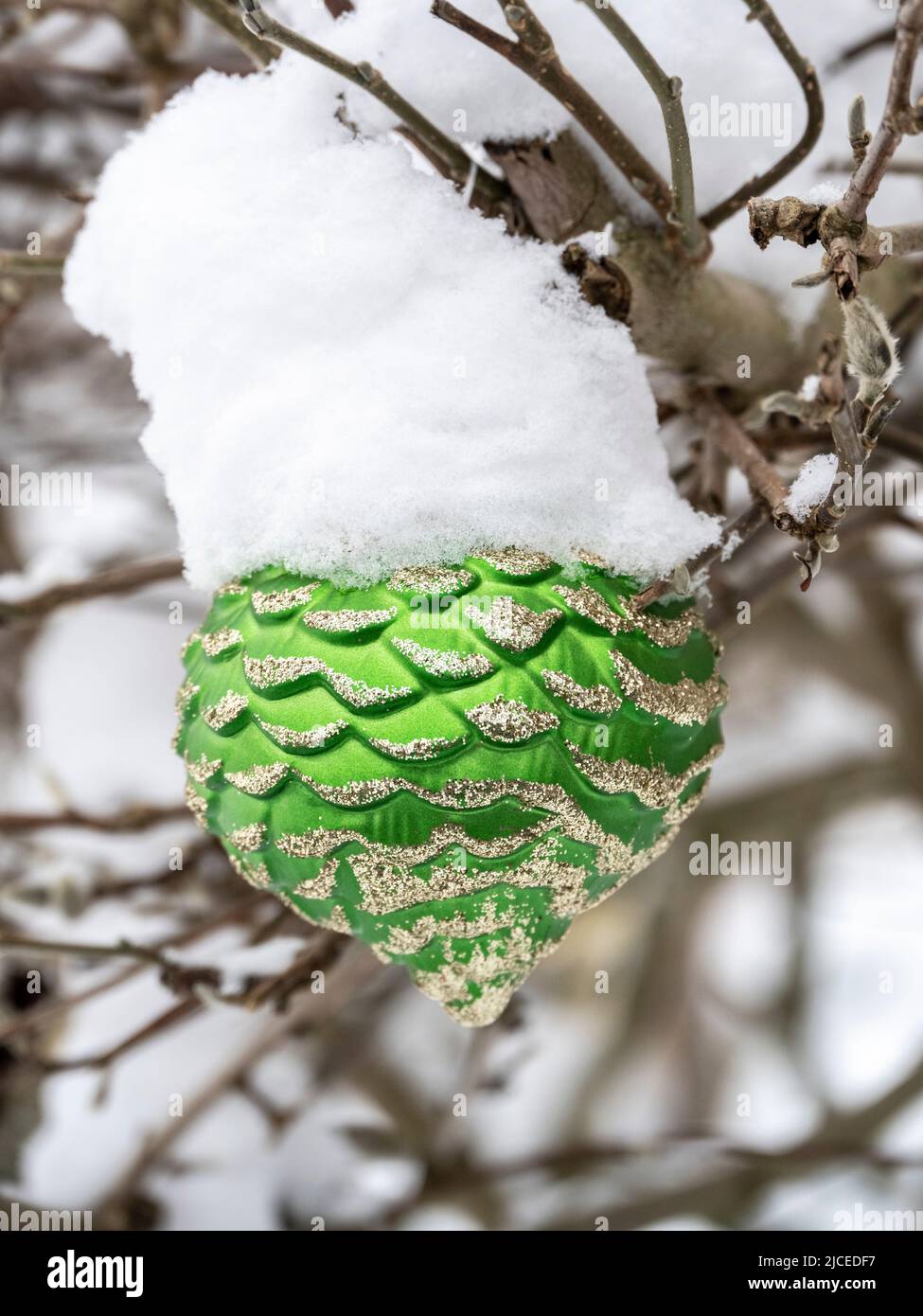 Ornamento natalizio con cono di pino verde appeso su un albero all'esterno coperto di neve Foto Stock