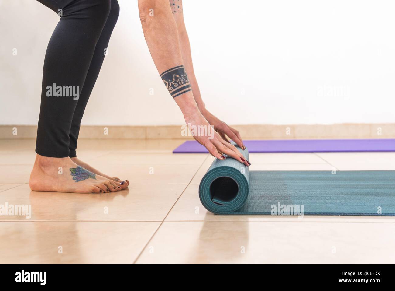 Dettaglio di una donna con tatuaggi sulle braccia e i piedi che rotolano su un tappeto yoga, mani che rotolano su un tappeto Foto Stock
