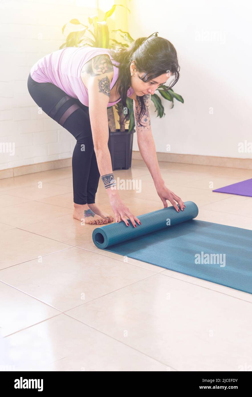 Foto verticale di una donna con tatuaggi che rotolano su un tappeto per la pratica dello yoga al mattino Foto Stock
