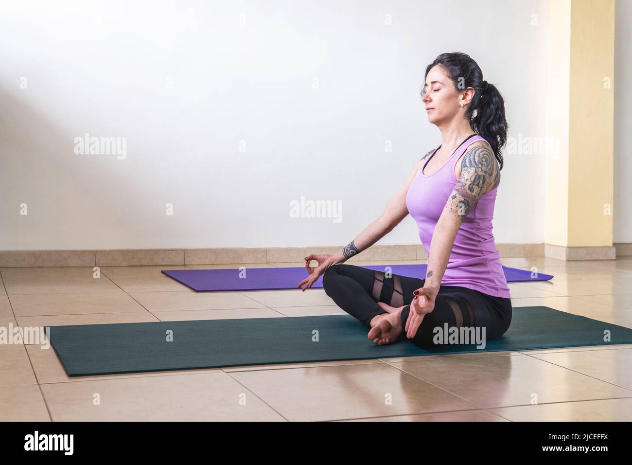 Donna latina seduta adulta con tatuaggi meditando e praticando yoga in posa padmasana Foto Stock