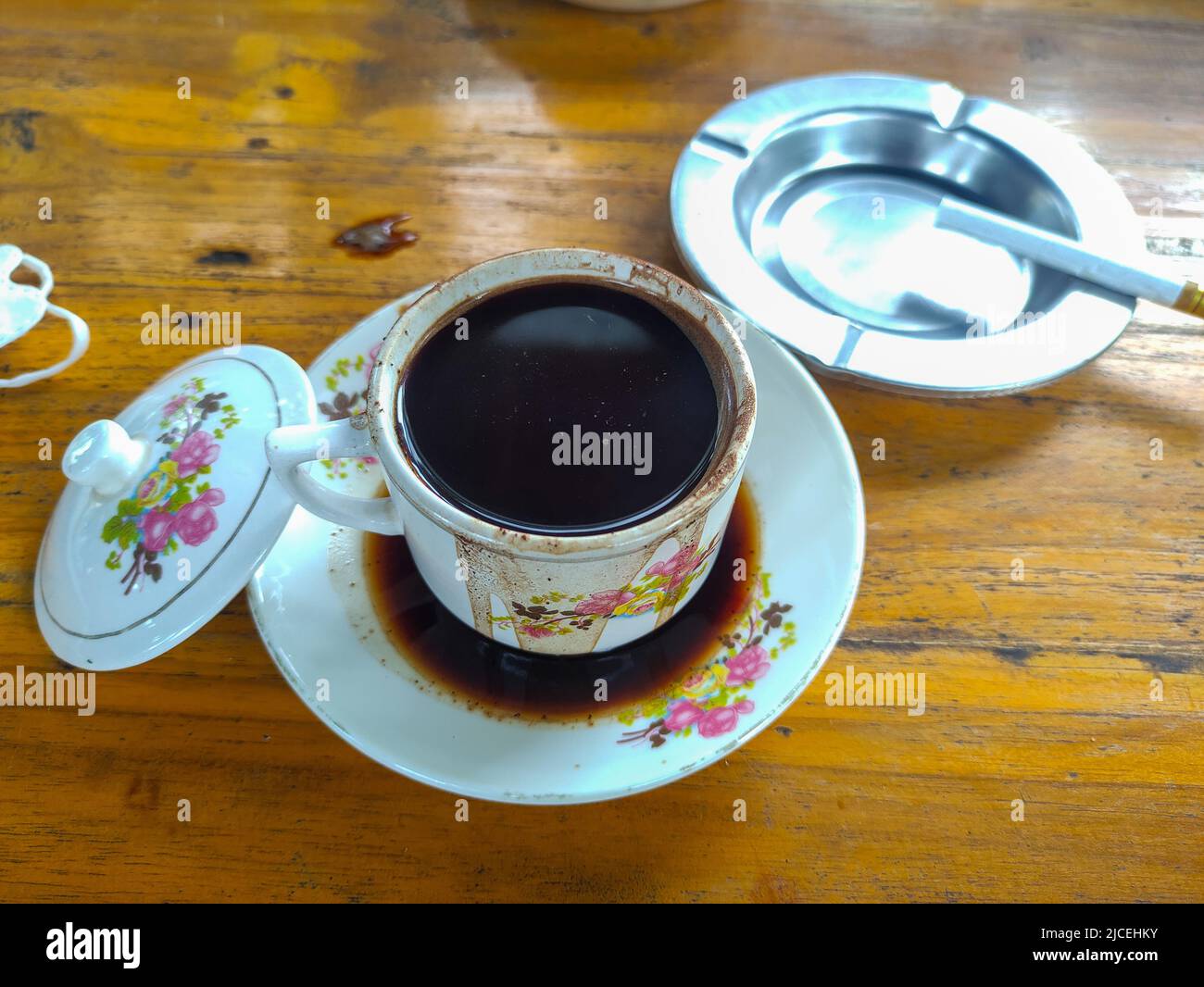 Tazza bianca di caffè caldo su sfondo di legno con posacenere e sigaretta Foto Stock