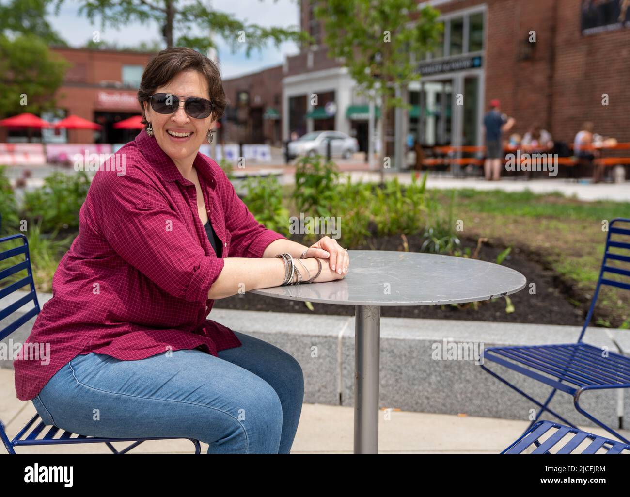 Felice, donna matura seduta ad un tavolo all'aperto da solo Foto Stock