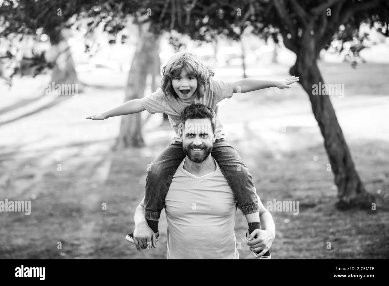 Felice padre che dà la spalla cavalcata sulle sue spalle in giardino. Figlio sulla spalla papà guardando la macchina fotografica. Attività per il fine settimana, concetto di stile di vita familiare Foto Stock