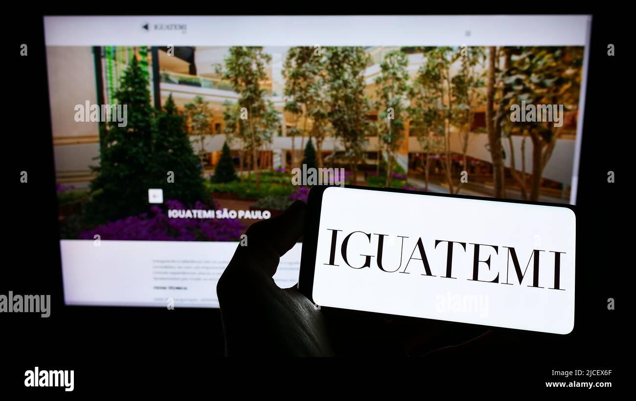 Persona che detiene smartphone con logo della società Iguatemi Empresa de Shopping Centers S.A. sullo schermo di fronte al sito web. Mettere a fuoco sul display del telefono. Foto Stock