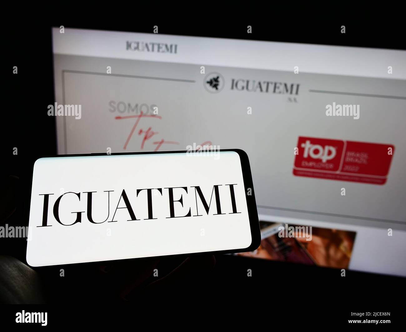 Persona che detiene il cellulare con il logo della società Iguatemi Empresa de Shopping Centers SA sullo schermo di fronte alla pagina web. Mettere a fuoco sul display del telefono. Foto Stock