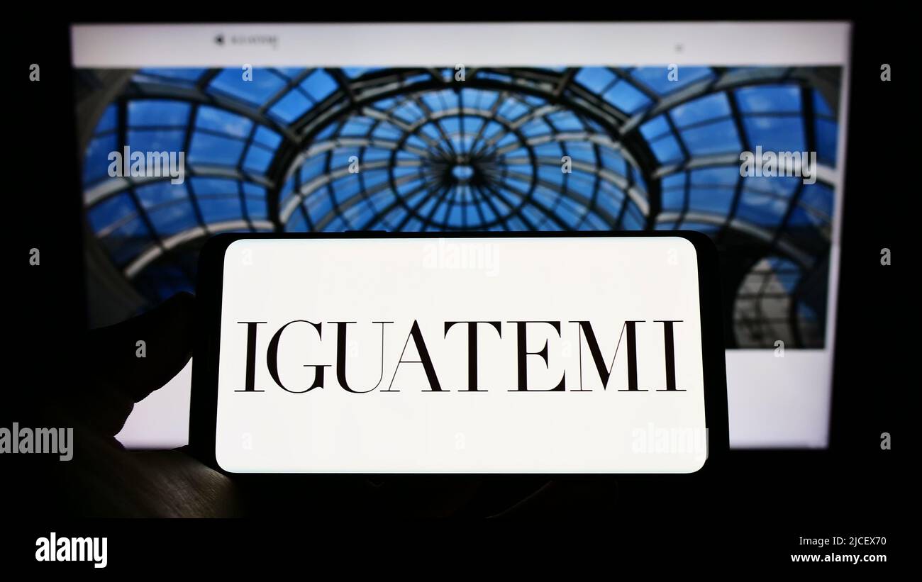 Persona che detiene il cellulare con il logo della società Iguatemi Empresa de Shopping Centres S.A. sullo schermo di fronte al sito web. Mettere a fuoco sul display del telefono. Foto Stock