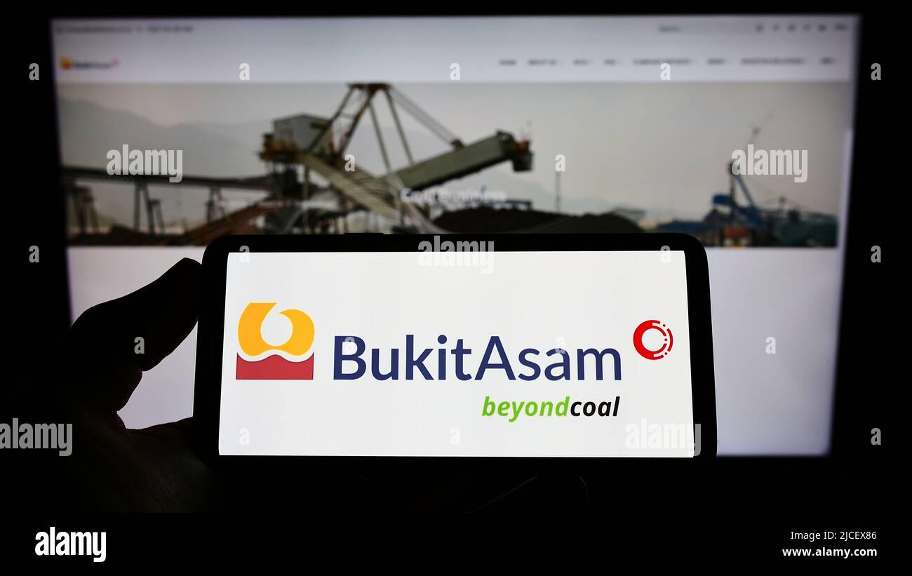 Persona che tiene smartphone con il logo della società mineraria indonesiana PT Bukit Asam Tbk sullo schermo di fronte al sito web. Mettere a fuoco sul display del telefono. Foto Stock