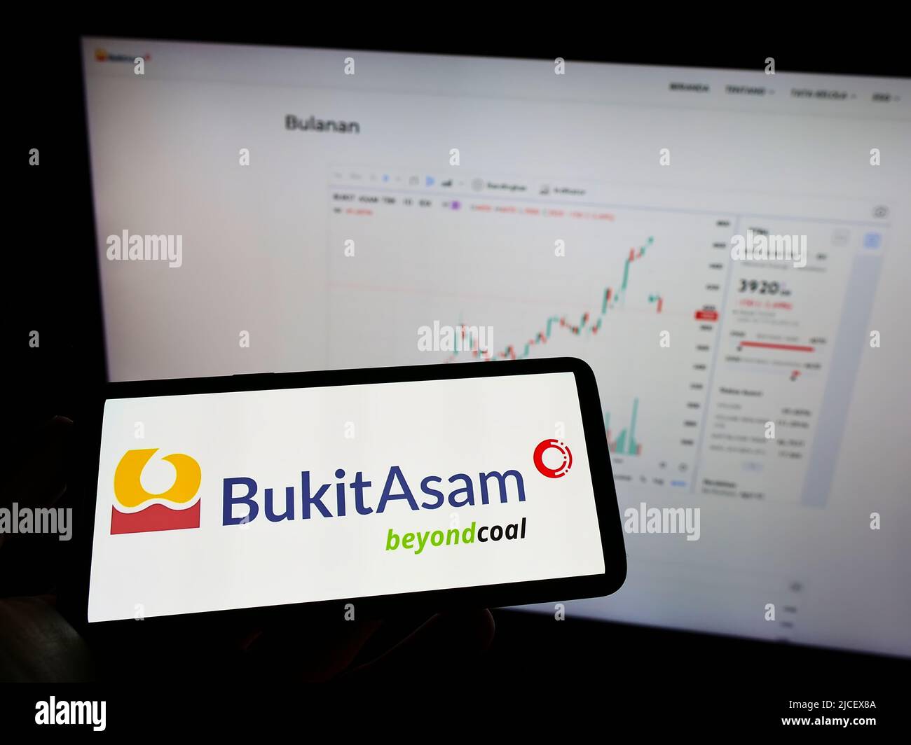 Persona che tiene il telefono cellulare con il logo della società mineraria indonesiana PT Bukit Asam Tbk sullo schermo di fronte alla pagina web. Mettere a fuoco sul display del telefono. Foto Stock