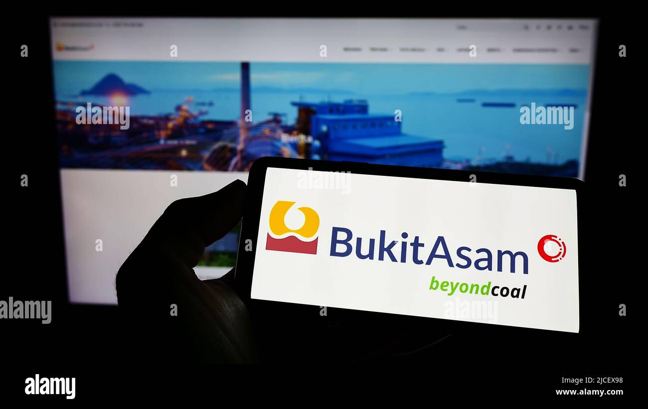 Persona che tiene il cellulare con il logo della società mineraria indonesiana PT Bukit Asam Tbk sullo schermo di fronte al sito web aziendale. Mettere a fuoco sul display del telefono. Foto Stock
