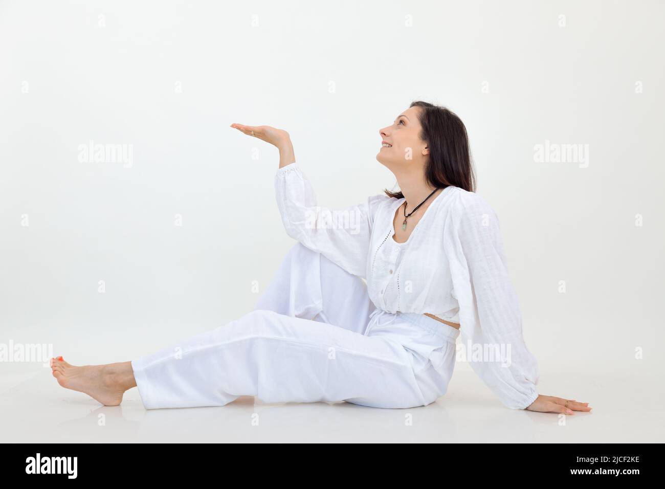 Bella sorridente e affascinante femmina seduta in bianco studio. Posizionare il testo sul palmo per inserire la pubblicità. Spazio di copia Foto Stock