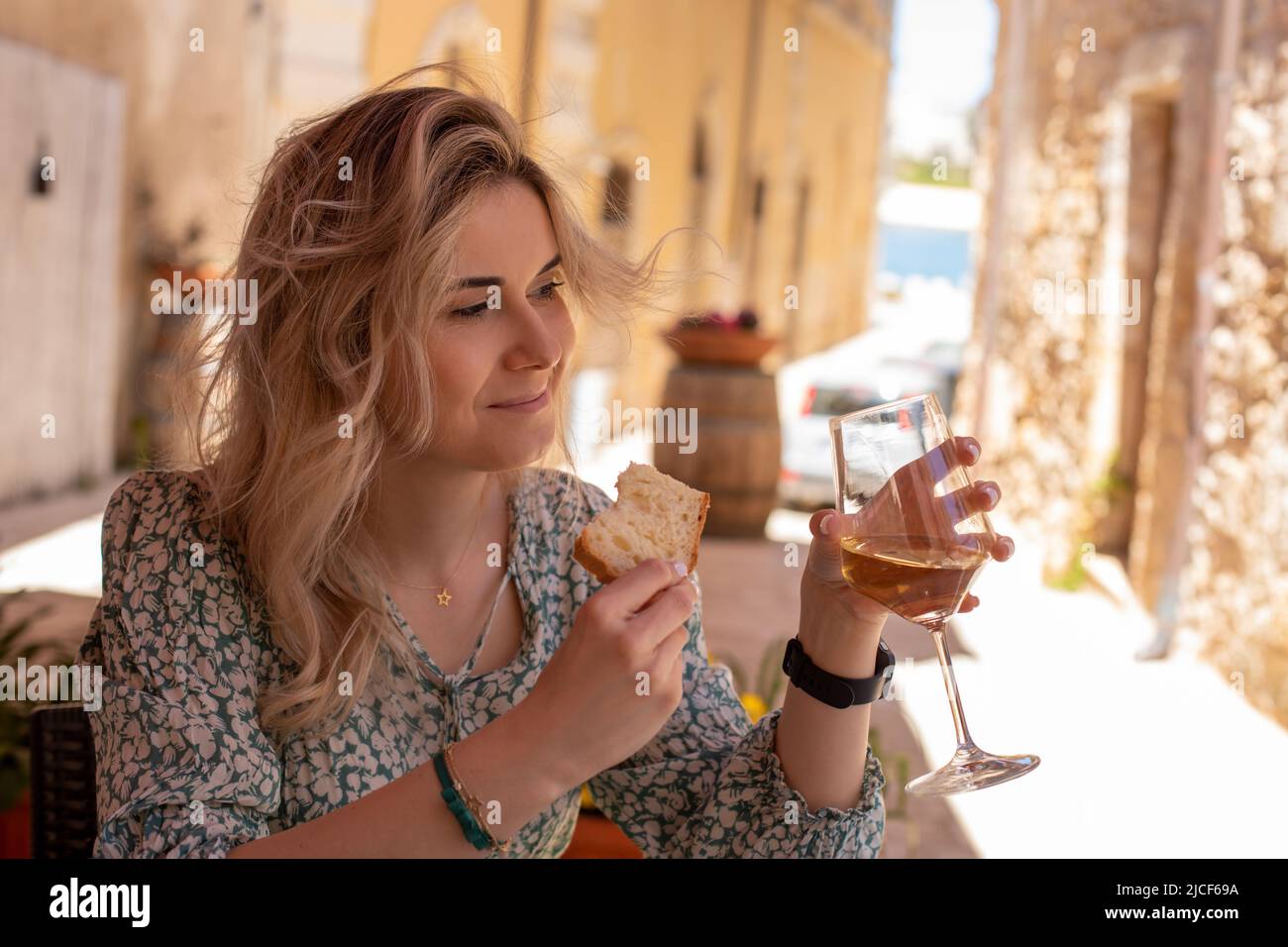 Ritratto di giovane donna splendida vestito estate, seduta, tenendo un bicchiere di vino bianco e pezzo di pane tostato. Foto Stock