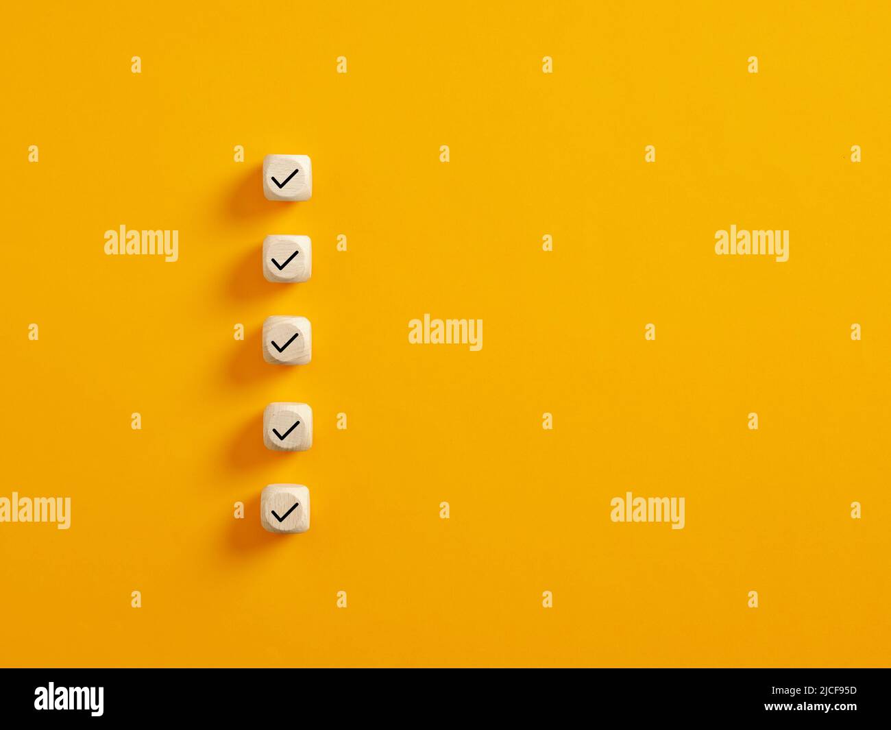 Cubetti di legno con segno di spunta su sfondo giallo, concetto Checklist con spazio di copia. Foto Stock
