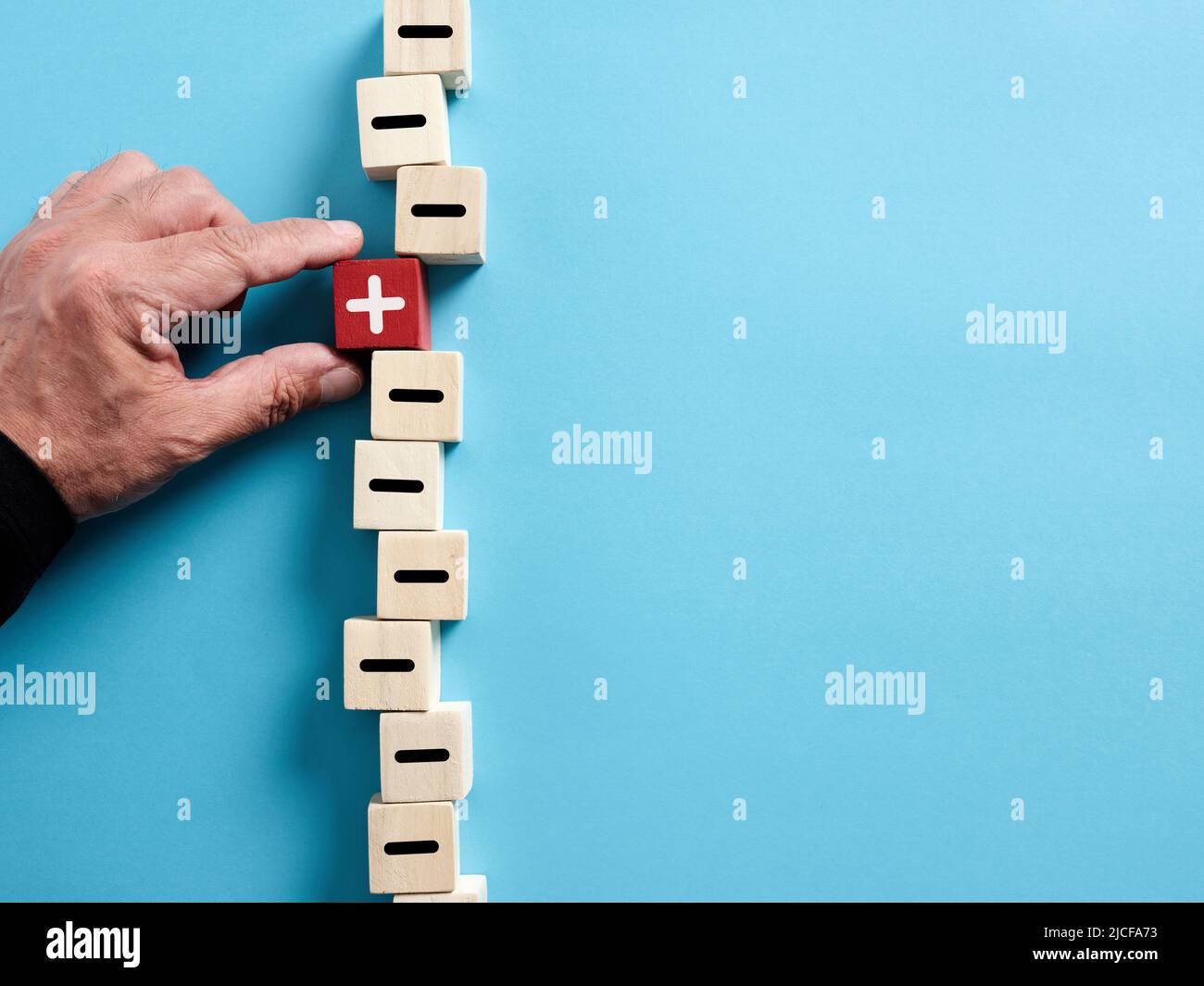 La mano maschio seleziona il cubo di legno con il simbolo più tra i cubi con le icone meno. Scegliere la giusta opzione positiva tra i negativi. Foto Stock