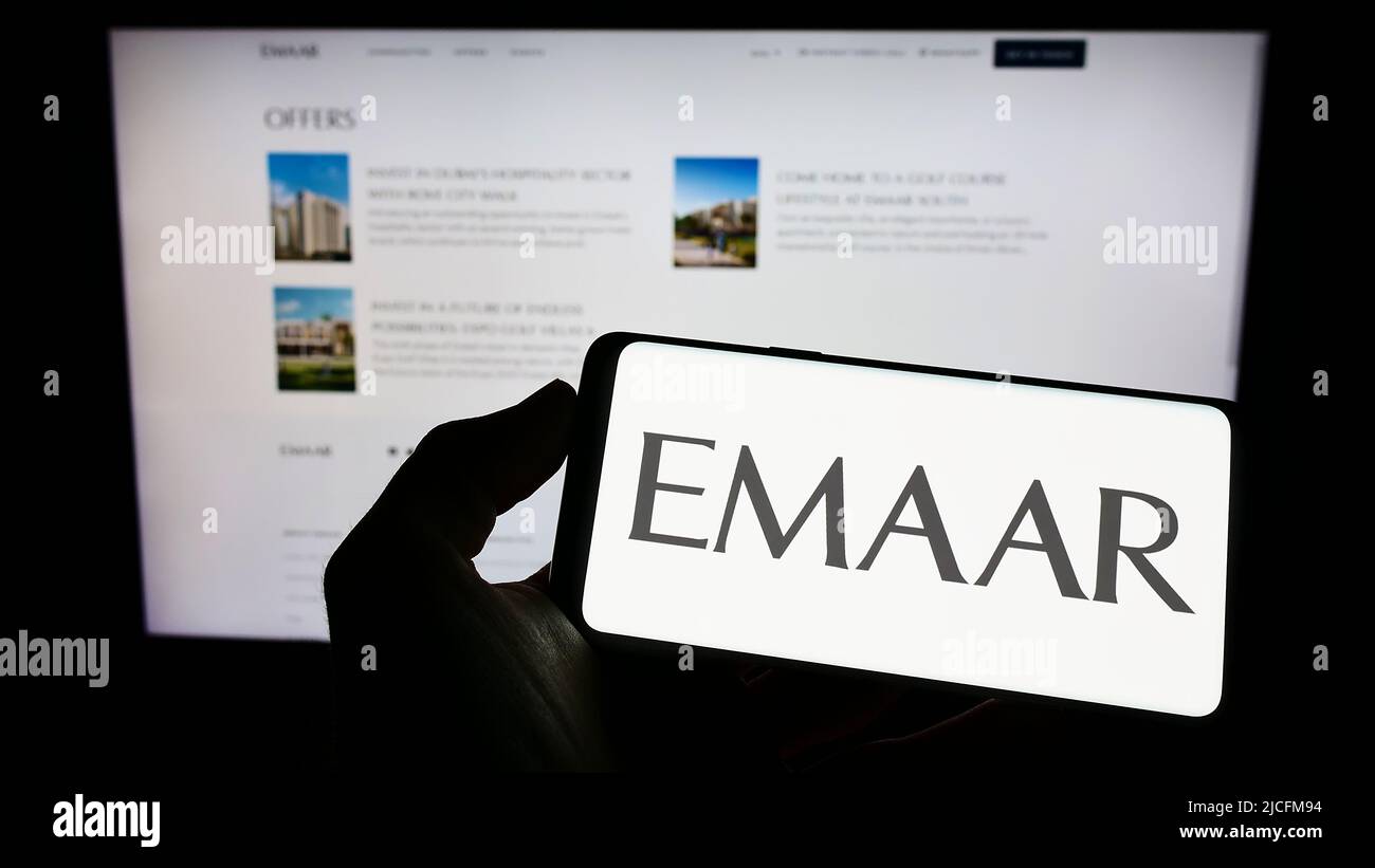 Persona che detiene il telefono cellulare con il logo della società immobiliare Emaar Proprietà PJSC sullo schermo di fronte al business web page. Mettere a fuoco sul display del telefono. Foto Stock