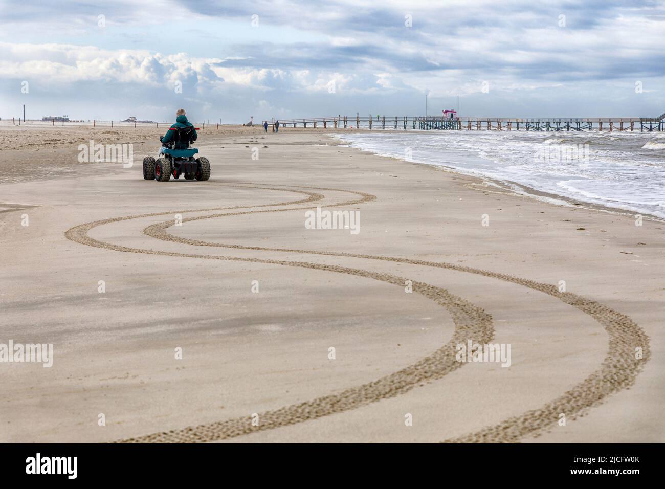 Uomo con handicap guidando linee a serpentina sulla spiaggia con la sua sedia a rotelle da spiaggia Foto Stock