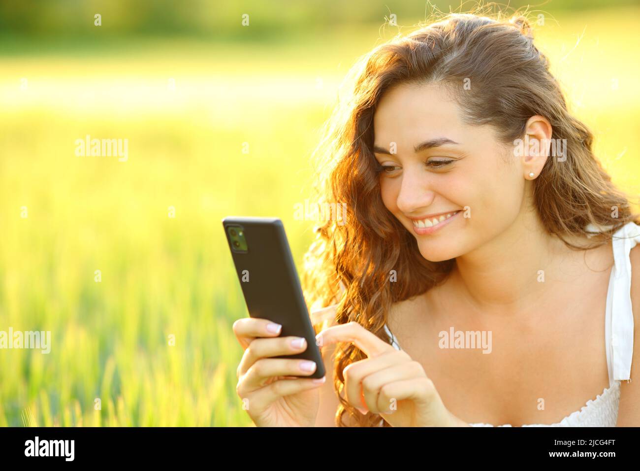 Donna felice che usa lo smartphone in un campo di grano al tramonto Foto Stock
