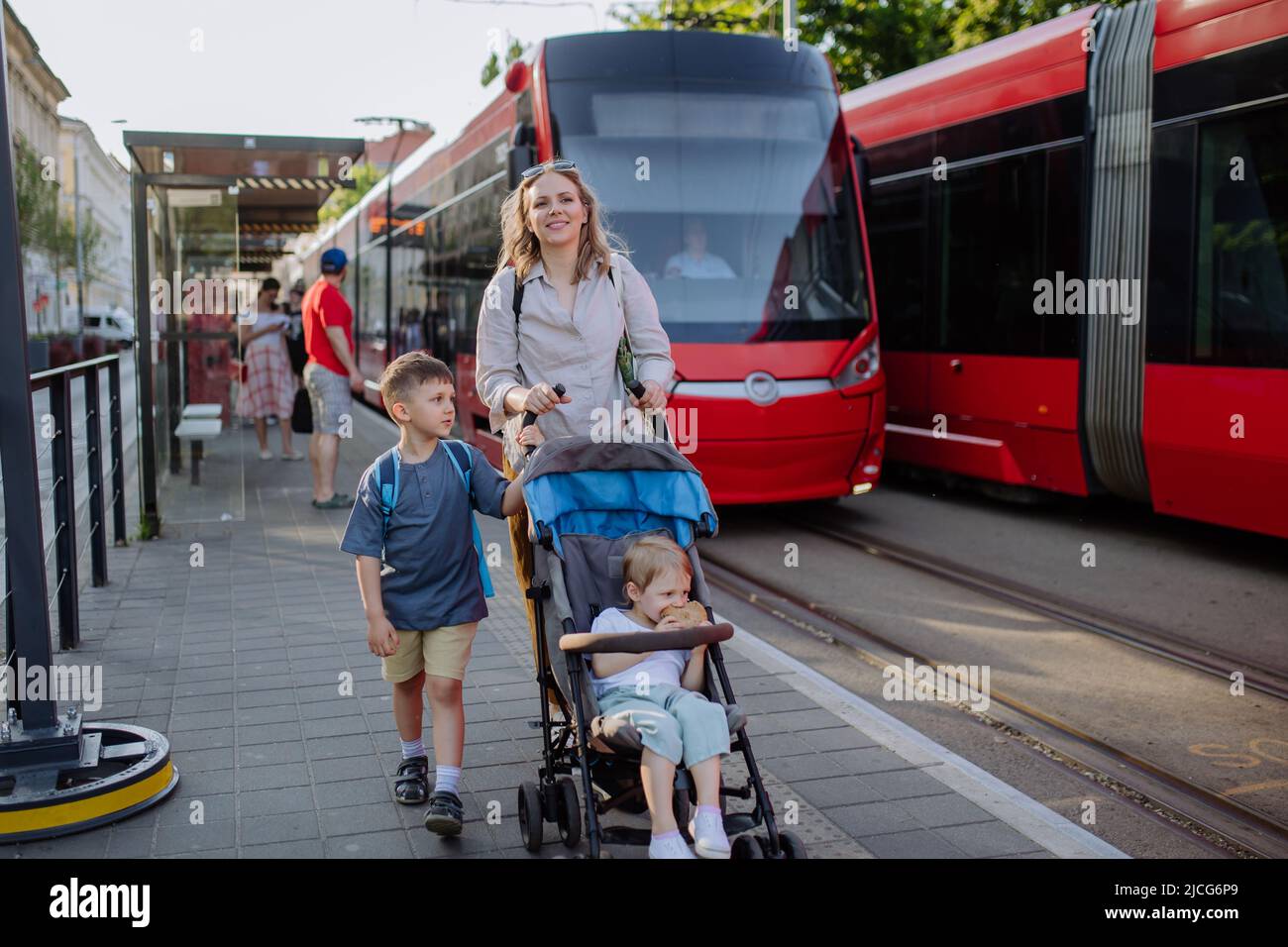 Giovane madre commuter con i bambini piccoli sulla strada per la scuola, a  piedi sulla stazione del tram in città Foto stock - Alamy