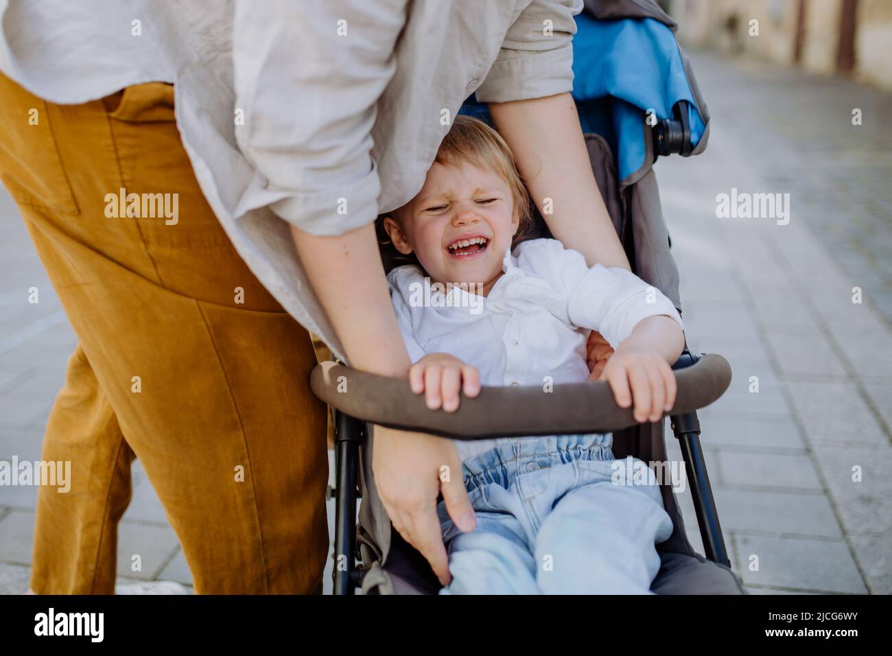 Madre calmante un bambino piangente seduto in un passeggino mentre cammina lungo la strada Foto Stock