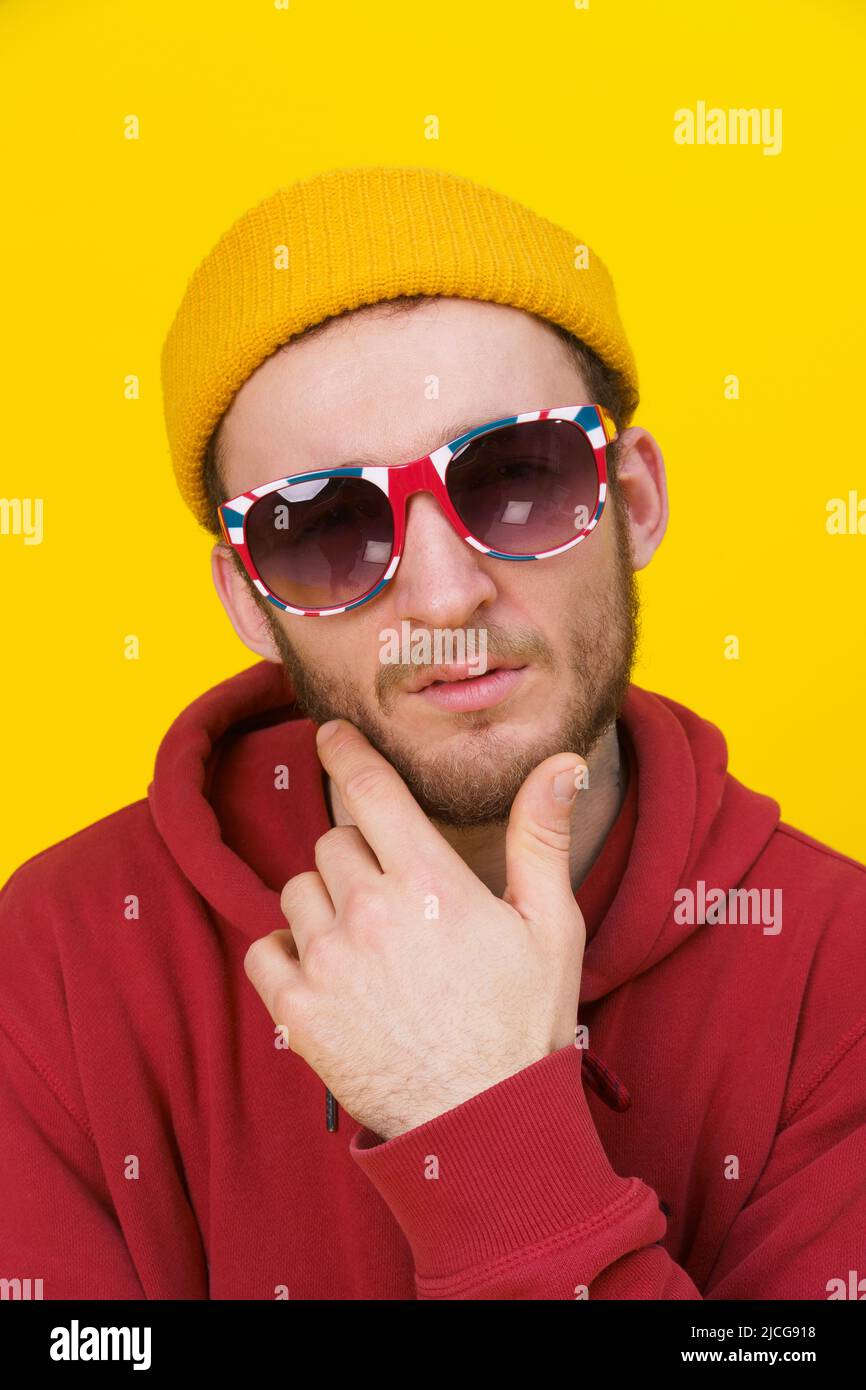 Ritratto di un giovane bel caucasico in abbigliamento casual, occhiali da sole guardando la macchina fotografica su sfondo giallo. Elegante look casual da uomo hipster dal bearded elegante. Ragazzo premuroso su sfondo giallo. Foto Stock