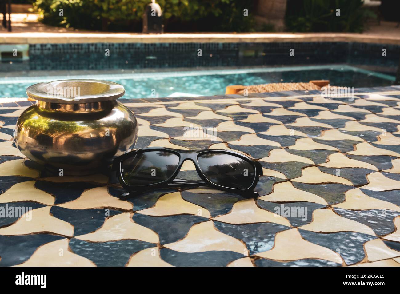 Occhiali da sole su un tavolo con una piscina sullo sfondo durante le vacanze. Foto Stock