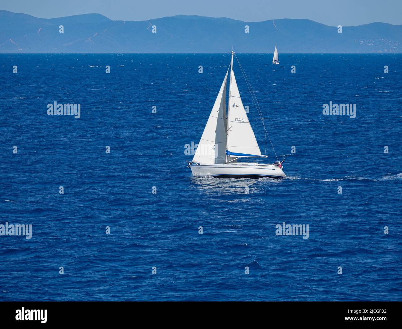 Barche a vela nell'arcipelago toscano, navigando tra la costa d'Elba e l'Italia continentale con montagne sullo sfondo. Foto Stock