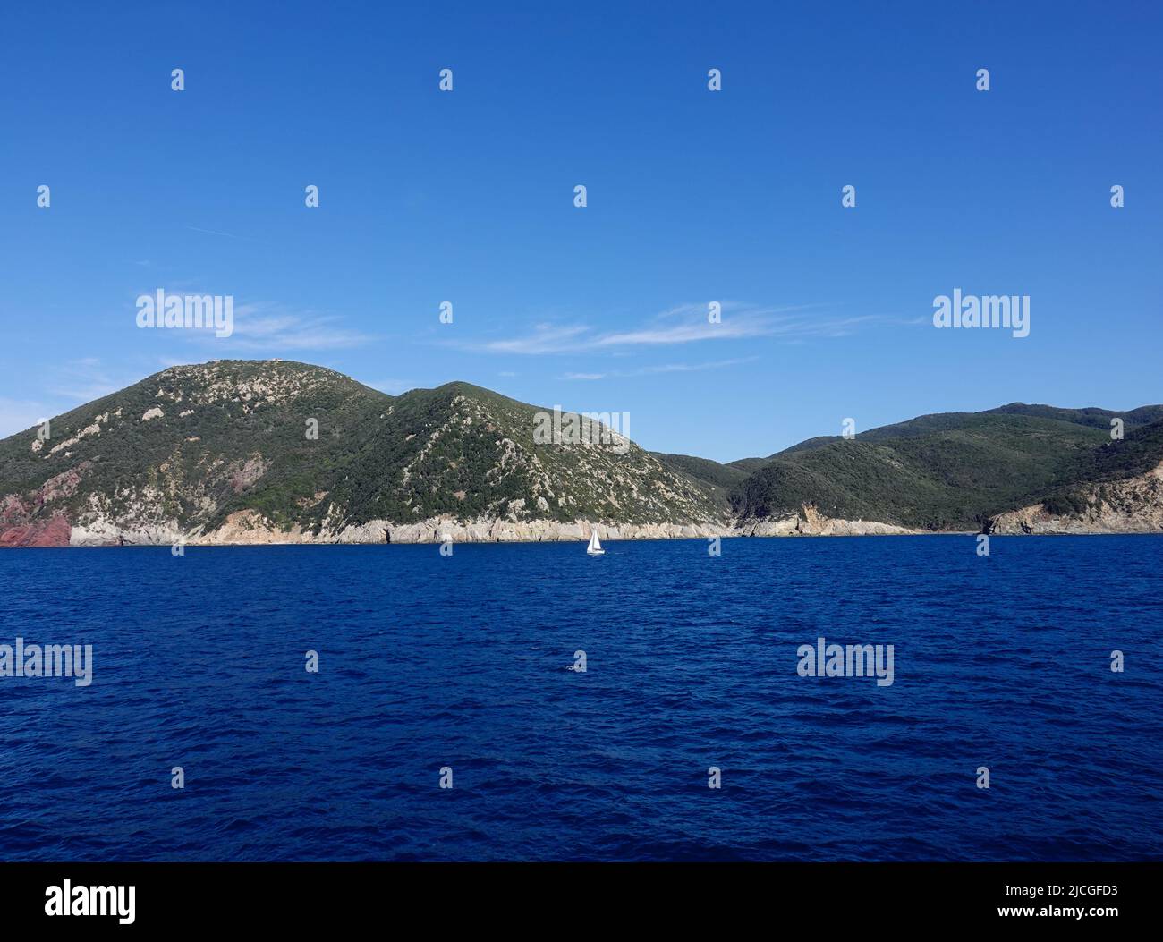 Paesaggio con barca a vela unica al largo della costa frastagliata dell'Isola d'Elba, Mar Ligure, Italia. Foto Stock