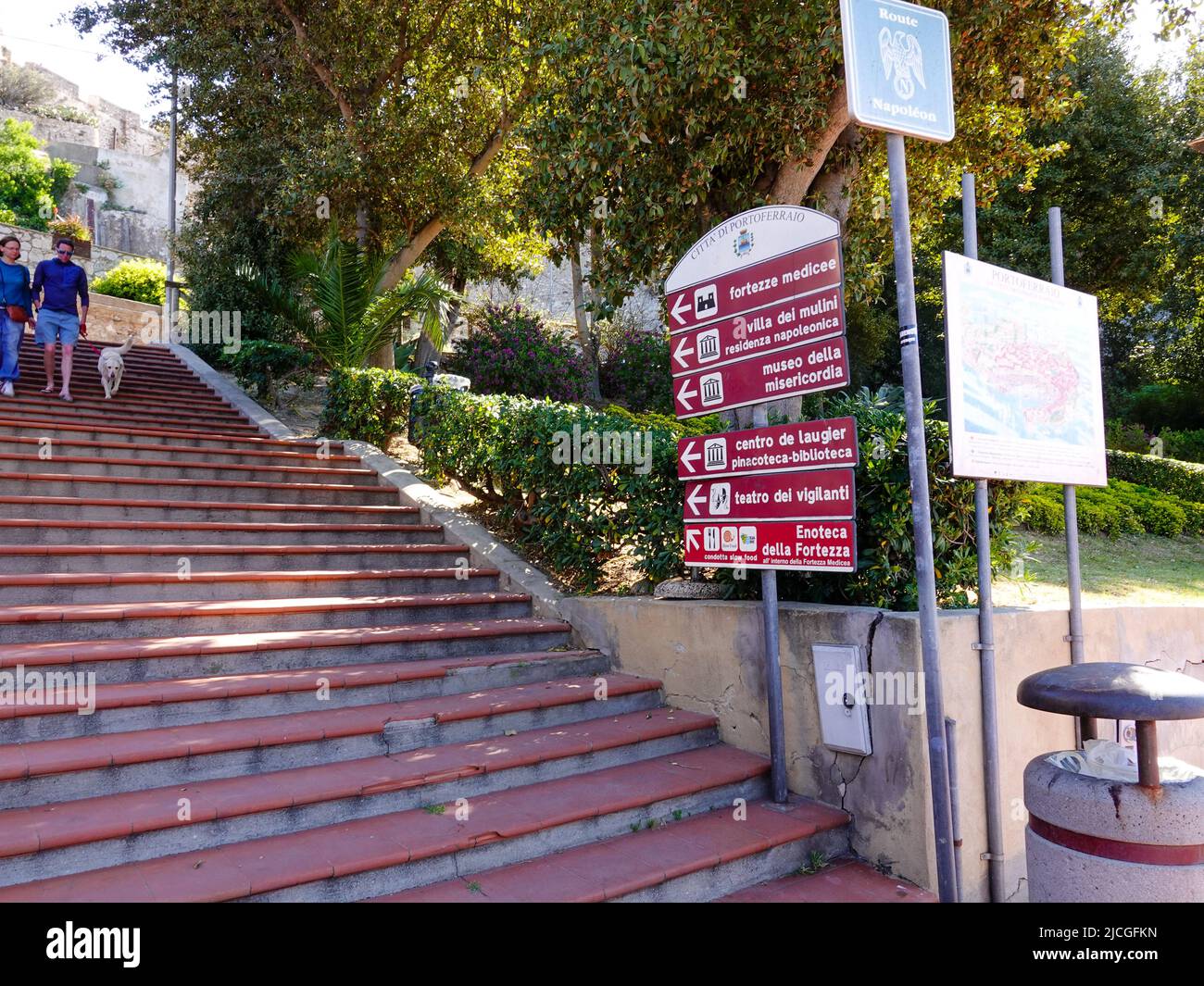 Persone che camminano lungo scalini e cartelli che indicano i siti storici come il Forte dei Medici e la Residenza di Napoleone, Portoreffaio, Elba, Italia. Foto Stock