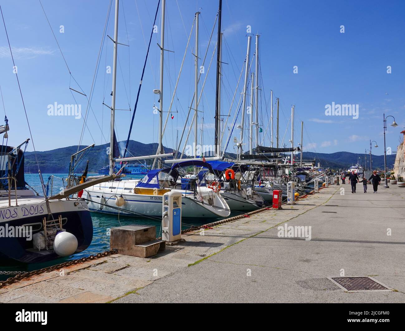 Persone che camminano lungo il Quai, passando per le barche ormeggiate al porto o Portoferraio sull'isola d'Elba, Toscana, Livorno, Italia. Foto Stock