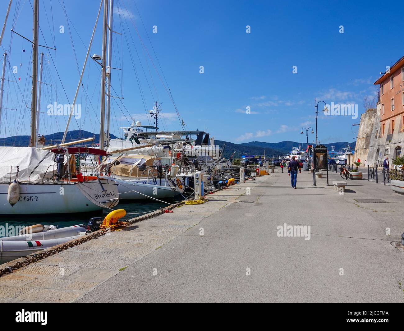 Persone che camminano lungo il Quai, passando per le barche ormeggiate al porto o Portoferraio sull'isola d'Elba, Toscana, Livorno, Italia. Foto Stock