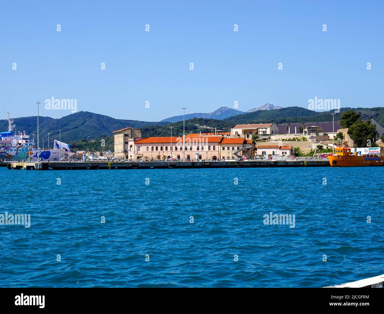 Edifici lungo la città portuale di Portoferraio, Isola d'Elba, Toscana, Italia, con colline, montagne sullo sfondo. Foto Stock