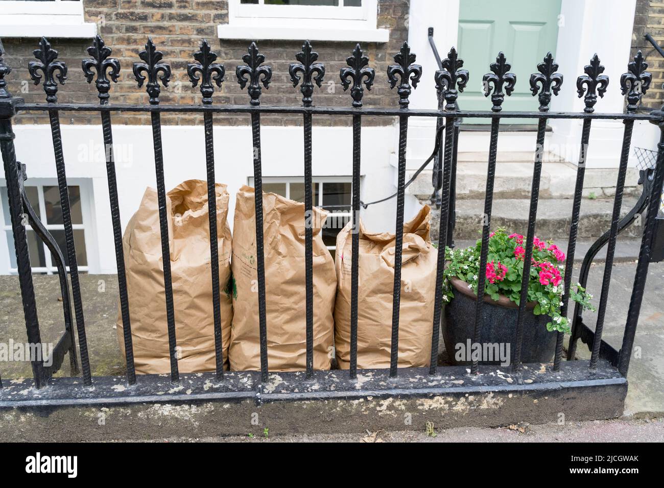 Riciclaggio di carta sacchi pieni di rifiuti da giardino pronti per la raccolta dietro le ringhiere di metallo nero da bin man Greenwich London Inghilterra UK Foto Stock