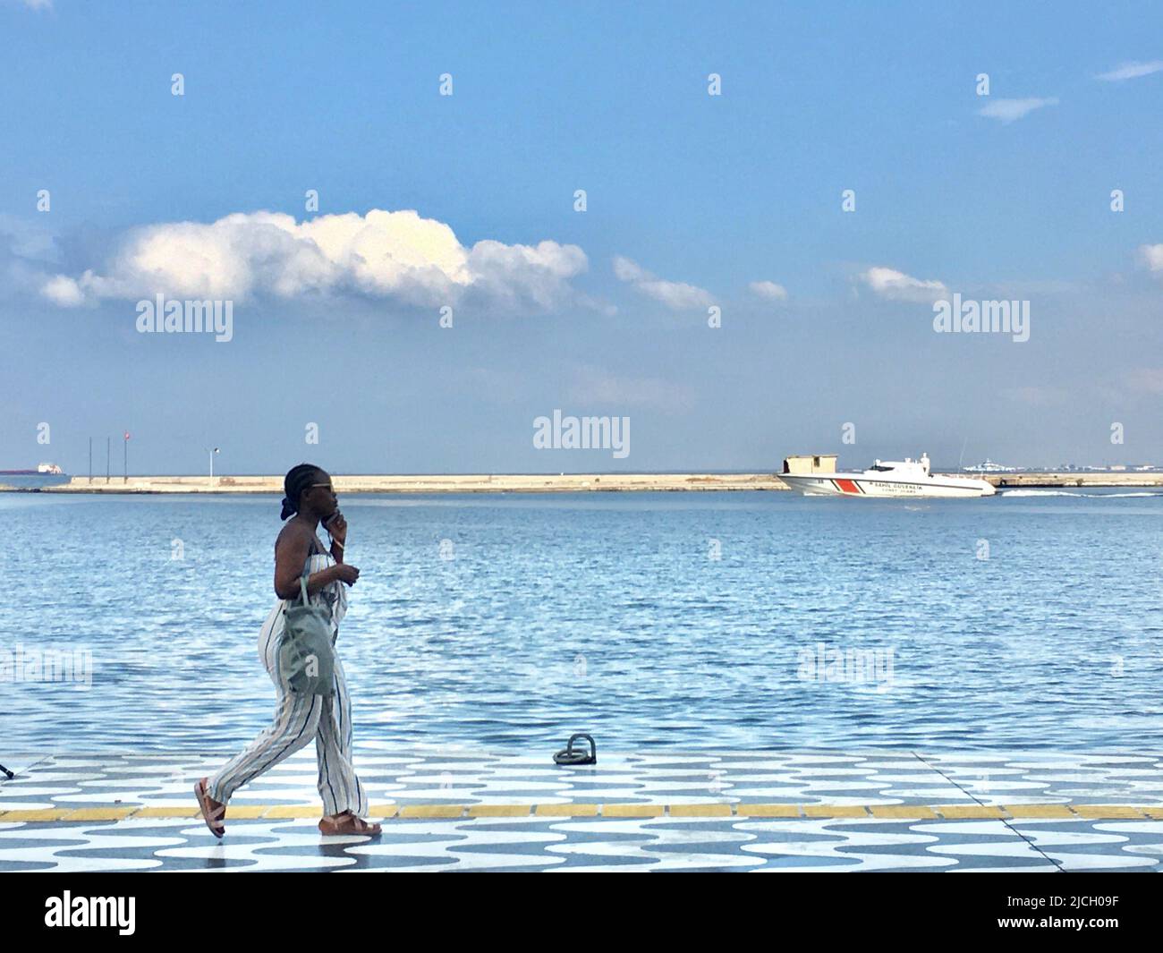 13 giugno 2022, Izmir, IzmÄ±r, Turkiye: Una donna africana cammina lungo il litorale di Izmir, mentre una guardia costiera turca naviga attraverso la baia di Izmir. La guardia costiera turca salva 55.000 migranti irregolari dal 2020 (Credit Image: © Uygar Ozel/ZUMA Press Wire) Foto Stock