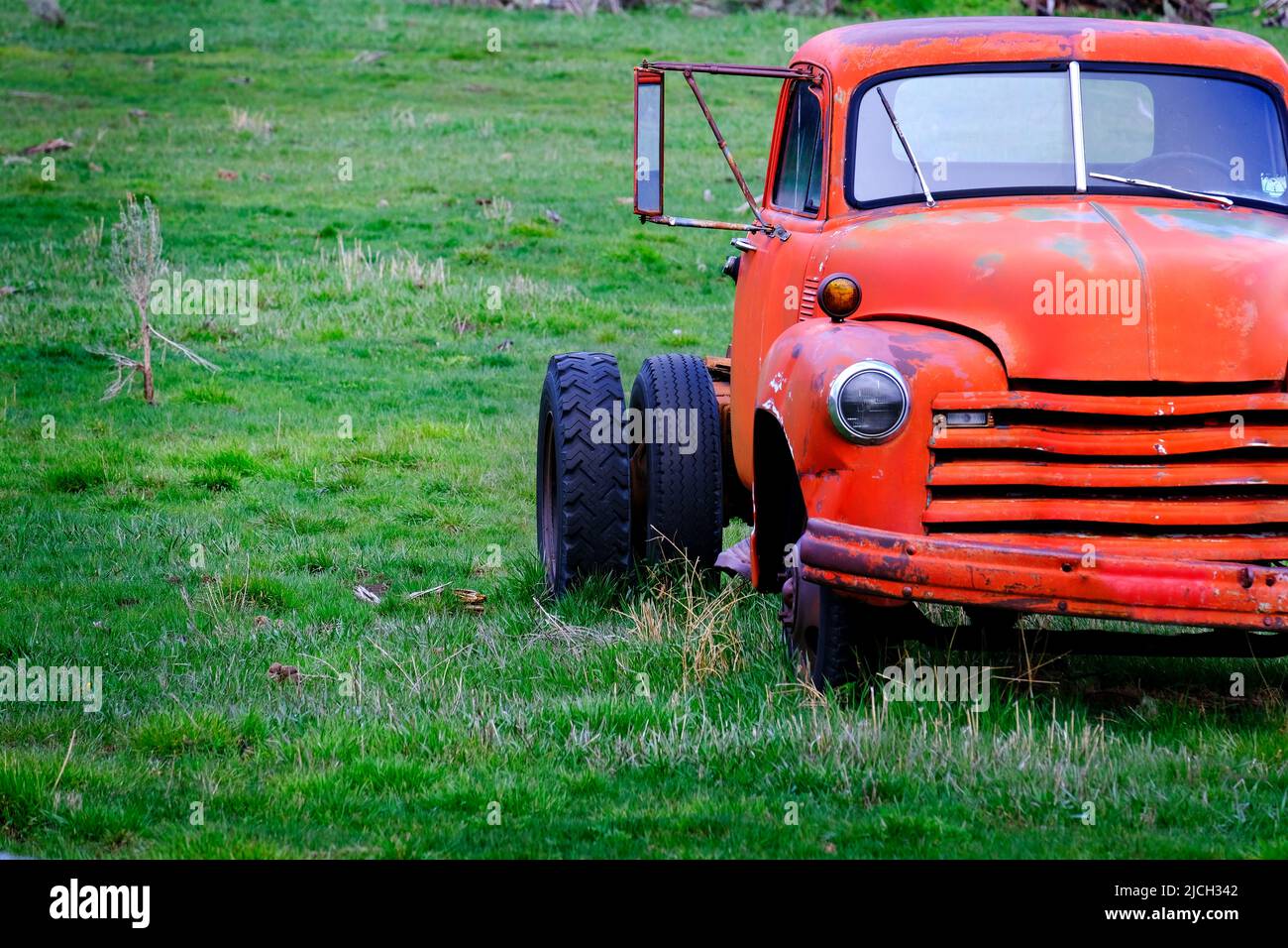 Vecchio camion da lavoro rosso funerato abbandonato in un campo verde fattoria Foto Stock