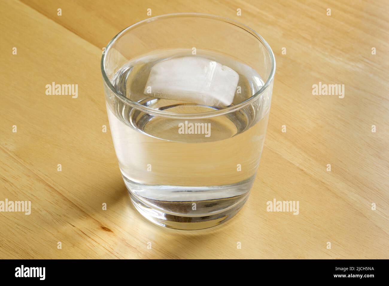 Un unico cubo di ghiaccio che si fonde e galleggia in un bicchiere d'acqua Foto Stock