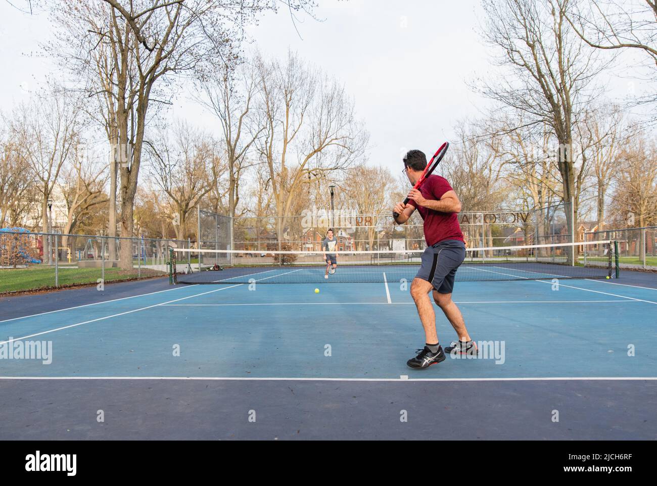 Uomo che gioca a tennis con figlio teen sul campo da golf all'aperto in primavera. Foto Stock