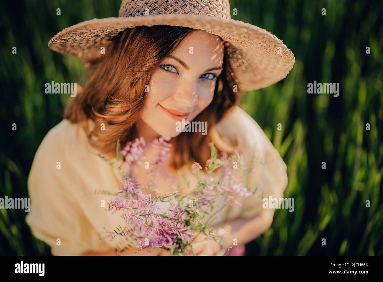 Graziosa donna di campagna in cappello di paglia con bouquet di fiori in campo. Foto Stock