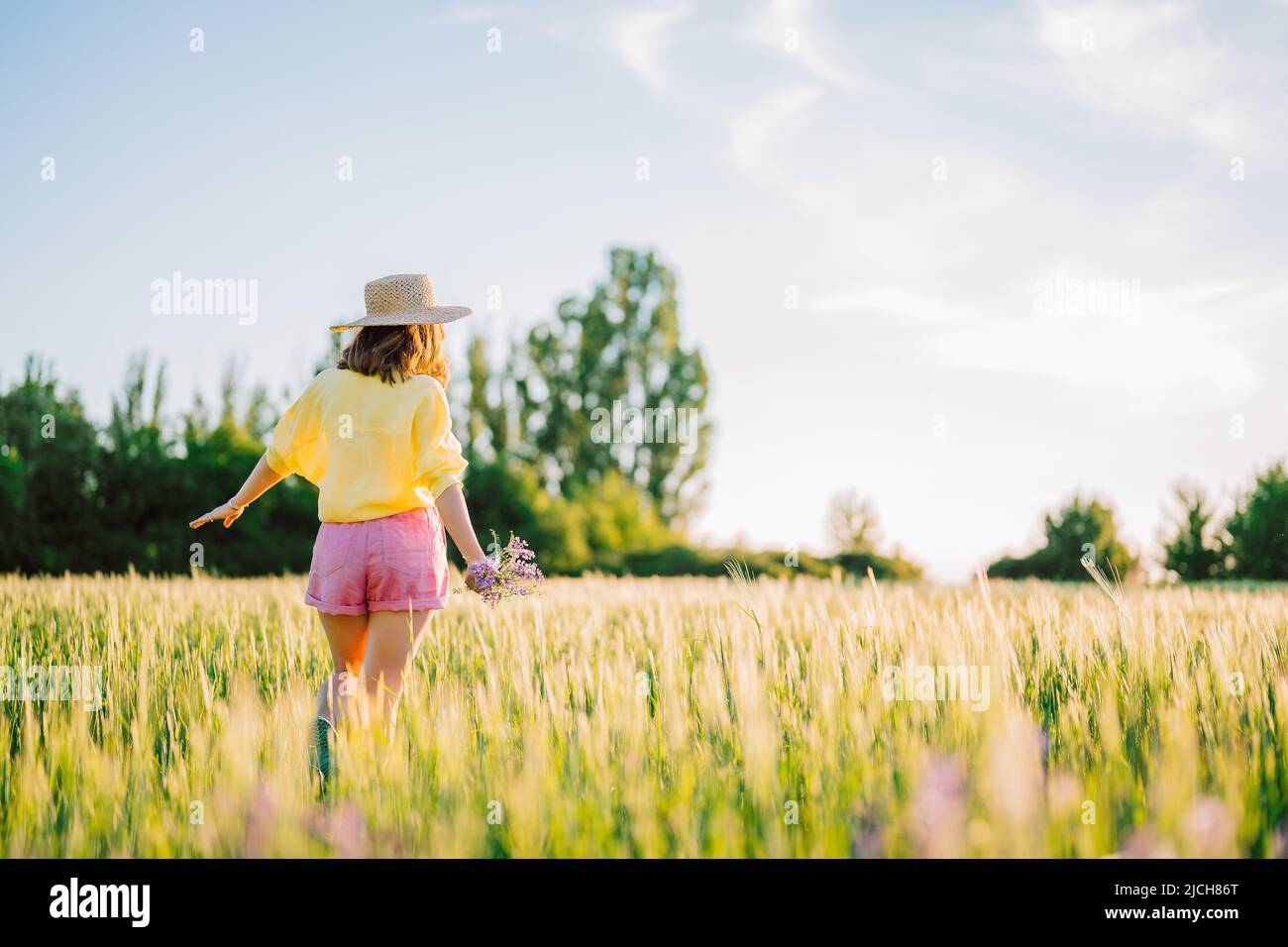 Bella donna di campagna in paglia cappello a piedi in campo di grano. Foto Stock