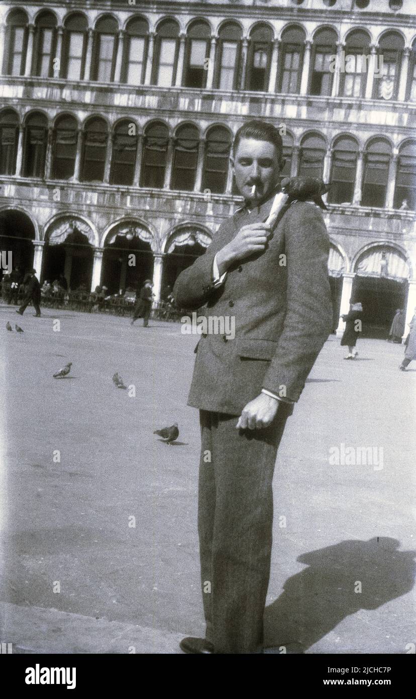 1930s, storico, piazza della città, possibile Roma, Italia, un gentiluomo in un abito doppio con un piccione sulla spalla mangiando il suo waffle o gelato. Foto Stock