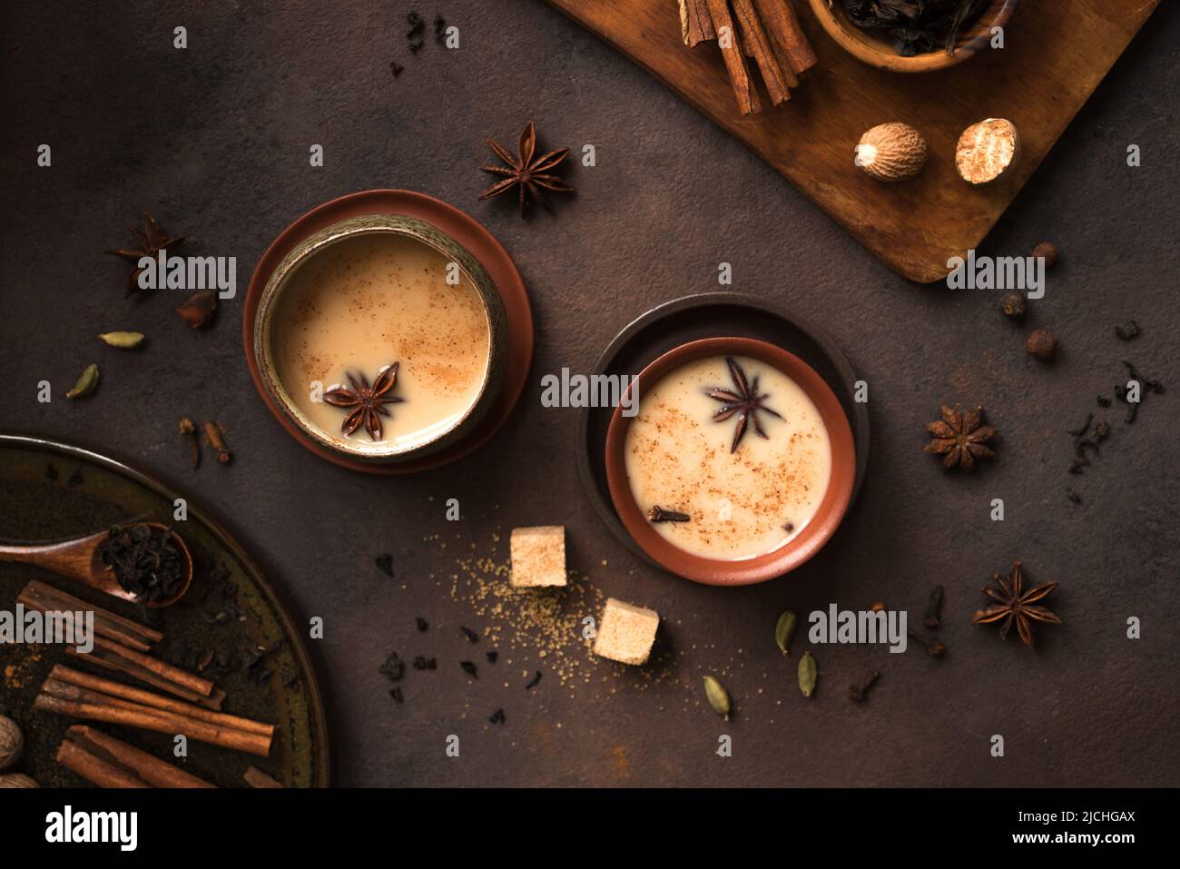 Masala Chai Tea in tazza di ceramica con ingredienti. Tradizionale tè nero speziato indiano con latte su sfondo rustico scuro Foto Stock