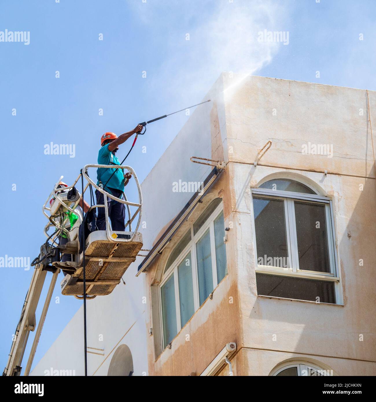 Un lavoratore su una gru, pulendo la polvere dal deserto sulla facciata di un edificio a Malaga. Foto Stock