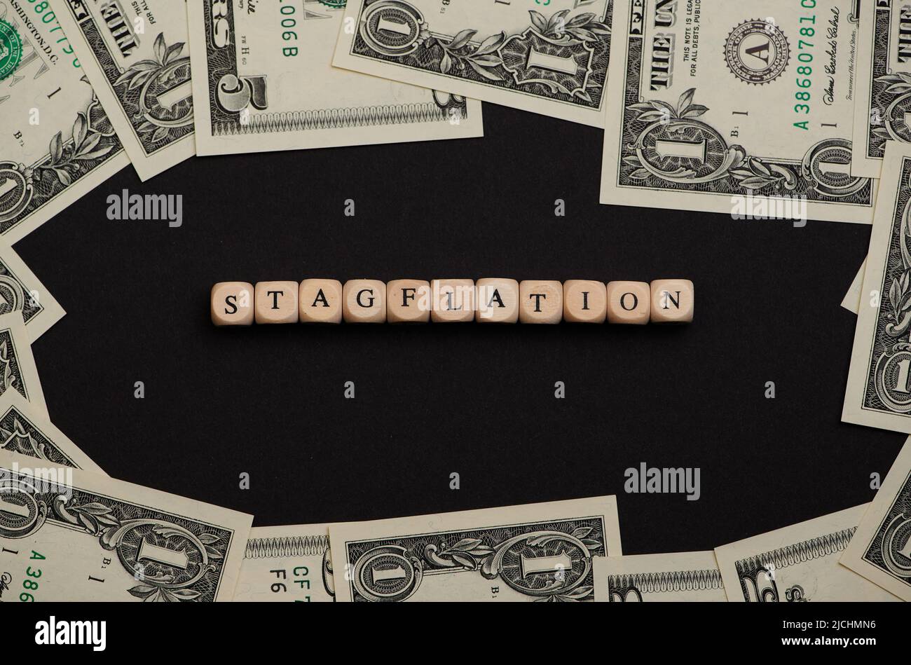 La parola stagflation posato con cubetti di legno su sfondo nero con banconote in dollari intorno Foto Stock