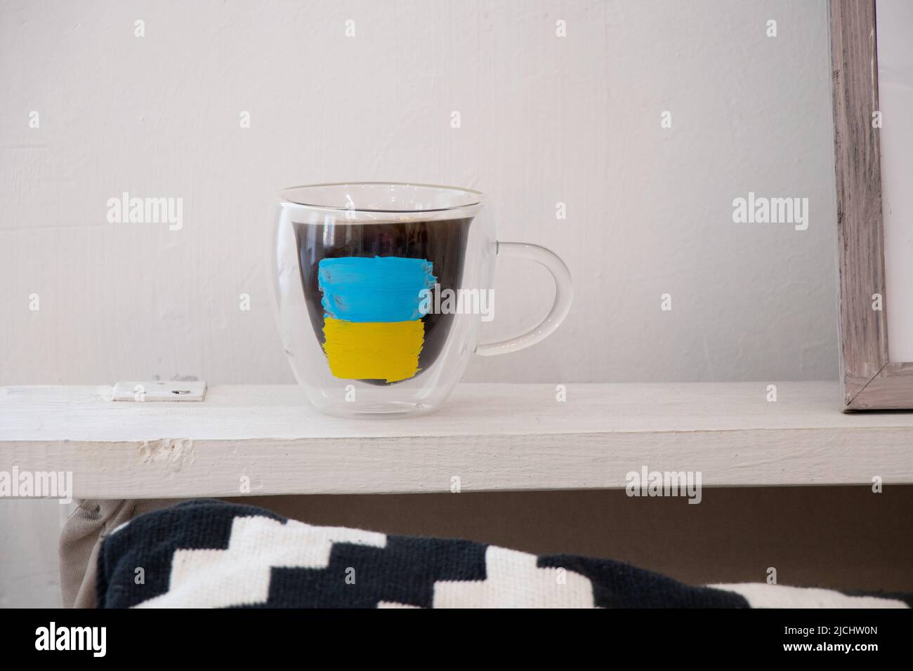 Una tazza di caffè si trova su una mensola a casa con una bandiera dipinta di Ucraina, guerra in Ucraina, un patriota del suo paese Foto Stock