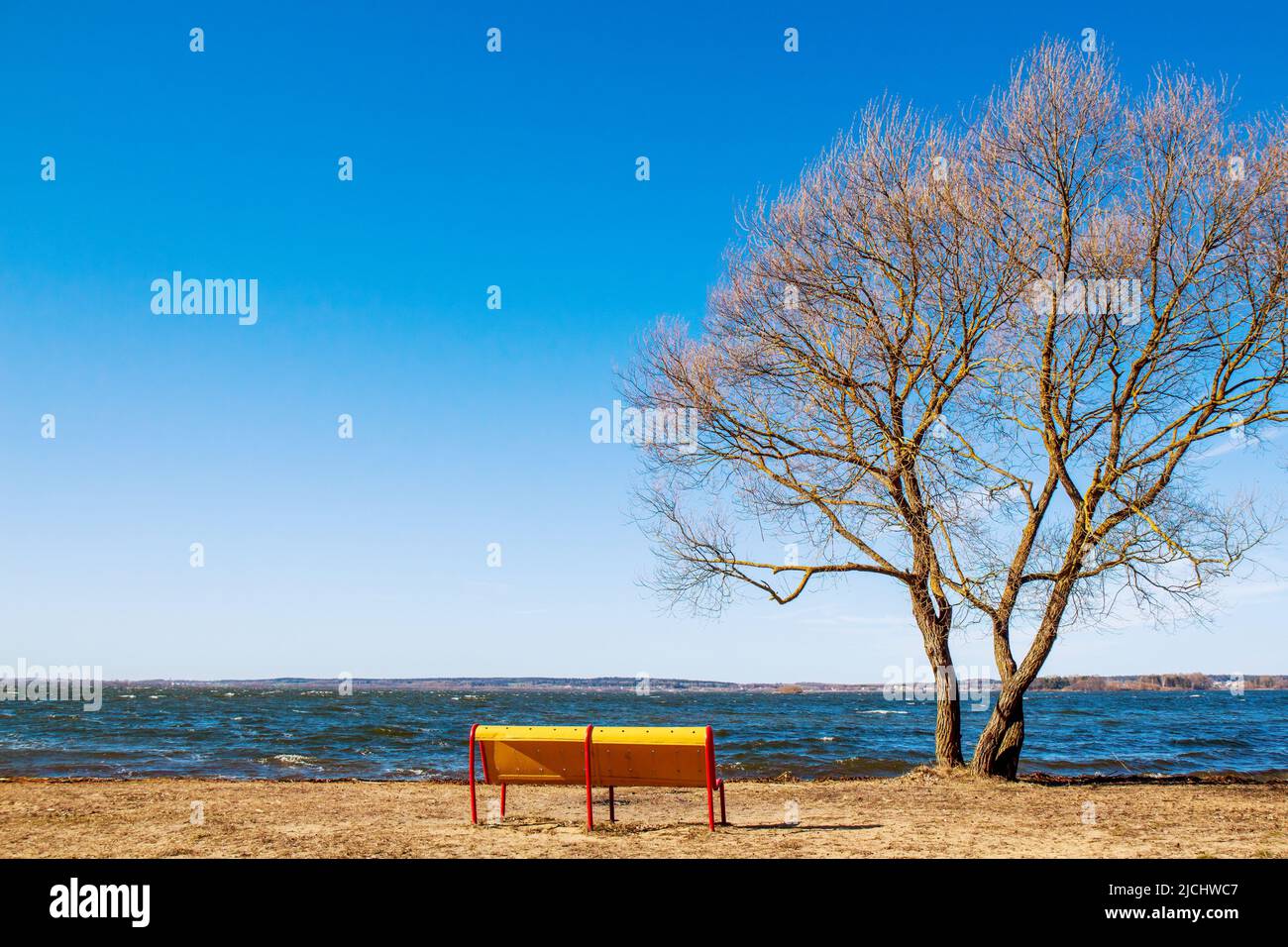 Una panca gialla vuota sulla riva di un grande serbatoio in una chiara e luminosa giornata di primavera. Vuoto Foto Stock