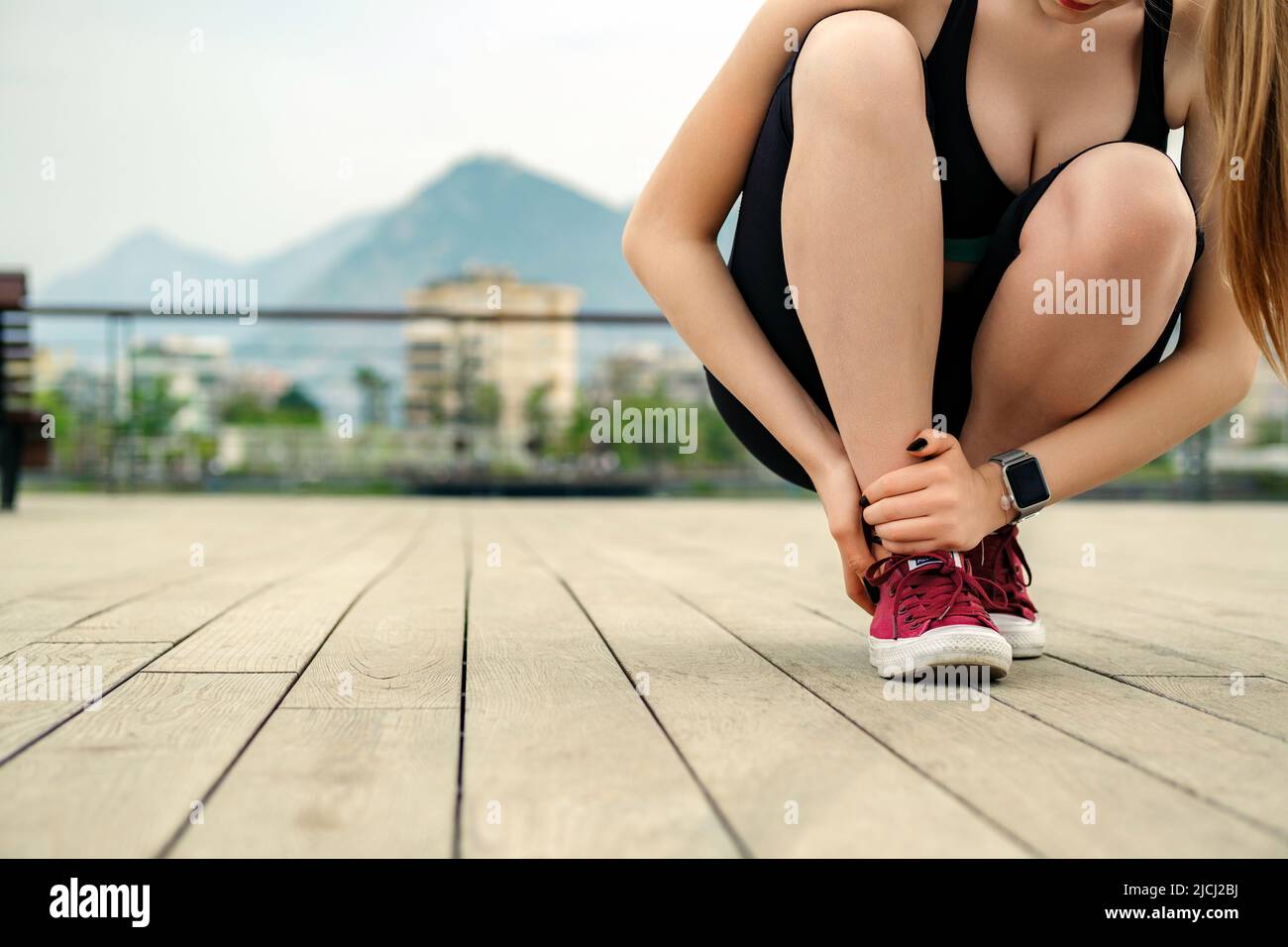 Donna sportiva bruna che indossa un reggiseno sportivo nero in piedi sul parco cittadino, all'aperto che soffre di una lesione alla caviglia durante l'esercizio e la corsa. Healthca Foto Stock